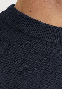 Navyblauwe gebreide sweaterstof met een geribde halslijn. De textuur is fijn en gelijkmatig, met gedetailleerde stiksels op de kraag.