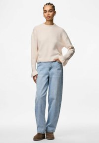 Jasnoróżowy sweter z dzianiny o szerokich rękawach, w połączeniu z luźnymi, jasnoniebieskimi dżinsami i brązowymi zamszowymi botkami za kostkę. Prosty design, miękka tekstura.