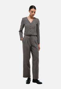 Costume à carreaux gris avec un blazer court, présentant un col en V et trois boutons, associé à un pantalon large taille haute et des chaussures noires.