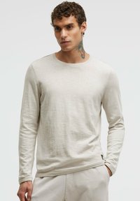 Helles beige Langarmshirt aus weichem Material, mit Rundhalsausschnitt, gerippten Bündchen und lockerer Passform. Dezente Textur ohne Muster.