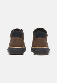 Botas de tobillo de ante marrón con acentos en negro y una suela acolchada. Presenta un detalle de logo y costuras en contraste alrededor de la suela.