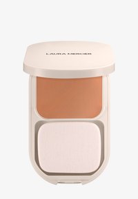 Polvo compacto con una sección de crema color beige encima de una esponja aplicadora blanca, alojado en un estuche redondo color crema con el nombre de la marca.