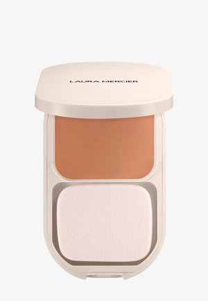 Poudre compacte comprenant une section de crème de couleur beige au-dessus d'une éponge applicatrice blanche, logée dans un boîtier rond crème portant le nom de la marque.