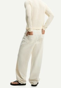 Pantalones blancos de gran tamaño con un corte holgado, que presentan dos bolsillos traseros y una textura suave, combinados con chanclas negras y un top de punto.