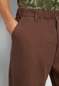 Bruna bomullsshorts med elastisk midja, sidofickor och platt fram. Tyget har en jämn textur och minimala designdetaljer.