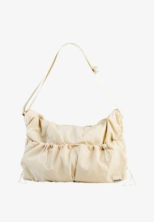 Sac à bandoulière beige réglable avec des poches à cordon et un petit patch logo "Bench." dans le coin inférieur droit.