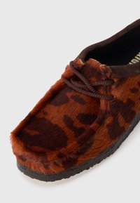 Brown fur slip-on shoe with a leopard print pattern, featuring a rounded toe, brown laces, and a textured black rubber sole.