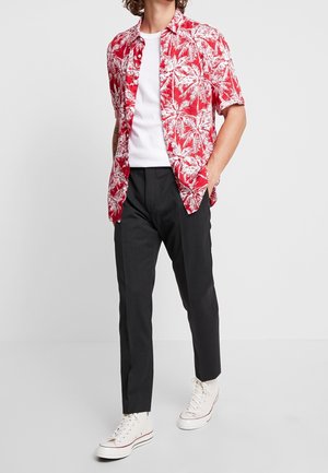 Camisa roja de manga corta con patrón de palmeras blancas, combinada con pantalones negros y zapatillas altas blancas.