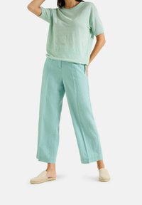 Licht muntgroene top met korte mouwen, gecombineerd met luchtige, wijdvallende muntgroene broek en neutrale instap espadrilles.