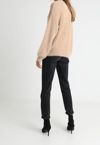 Lichtbeige donzige trui met lange mouwen, gecombineerd met donkere slim-fit jeans en zwarte enkellaarsjes, gezien van achteren.