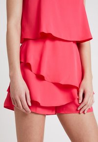 Vestido de capas en un rosa brillante, con un diseño fluido y volantes. Hecho de una tela ligera, tiene una textura suave.