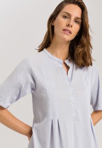 Camicia azzurra chiara a maniche corte con colletto rotondo, bottoni frontali e un design plissettato in vita. Tessuto morbido.