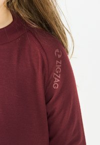 Bordeaux sweatshirt met een ronde hals, textuur op de schoudernaad en het "ZIGZAG" logo gedrukt in een lichtere tint op de mouw.