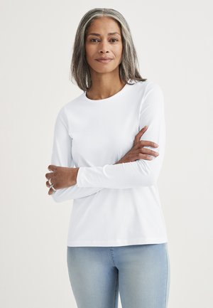 Vit långärmad skjorta i bomull med rund halsringning, mjuk textur och avslappnad passform, kombinerad med ljusblå denimjeans.