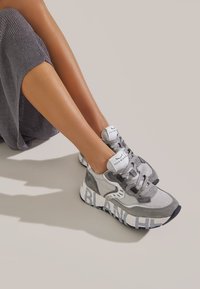 Graue Sneakers aus Mesh- und Wildledermaterialien, runde Zehenpartie, flache Schnürsenkel und fetter "BLANC"-Text auf der Sohle.