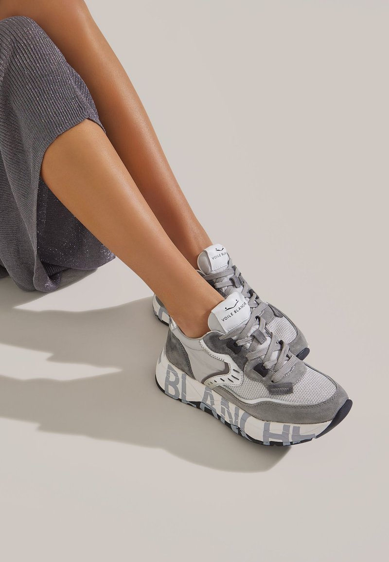Graue Sneakers aus Mesh- und Wildledermaterialien, runde Zehenpartie, flache Schnürsenkel und fetter "BLANC"-Text auf der Sohle.
