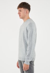 Maglione lavorato a maglia grigio chiaro con scollatura tonda, polsini e bordo a coste. Tessuto morbido e design aderente, presentato in una vista laterale su uno sfondo bianco.