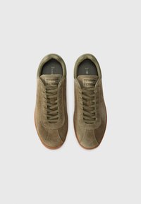 Adidași din suede verde măslin cu suprafețe texturate, șireturi plate și talpă din cauciuc. Prezintă un logo al brandului pe limbă și un guler căptușit.
