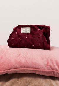 Manta de forro burdeos con bordado floral, doblada y colocada sobre un cojín de felpa rosa, mostrando una suave textura y un rico contraste de colores.