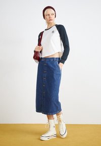 Crop long-sleeve shirt in white and navy, paired with a high-waisted denim skirt, featuring buttons down the front, and white high-top sneakers.