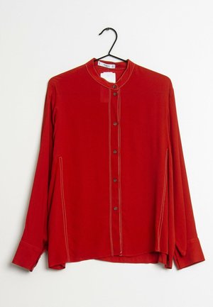 Red long-sleeve button-up blouse with beige stitching, round collar, hanging on a black hanger against a white background.