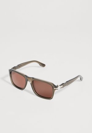 Lunettes de soleil de forme carrée avec montures translucides marron et verres marron foncé sur fond blanc.