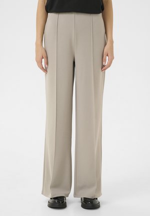 Beige wide-leg trousers made of soft fabric, featuring a high waist and vertical seam details, paired with black shoes.