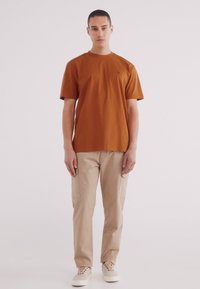 Korte mouw, roestkleurig katoenen t-shirt gecombineerd met beige cargobroek. Canvas sneaker compleet de outfit, met een strakke uitstraling.