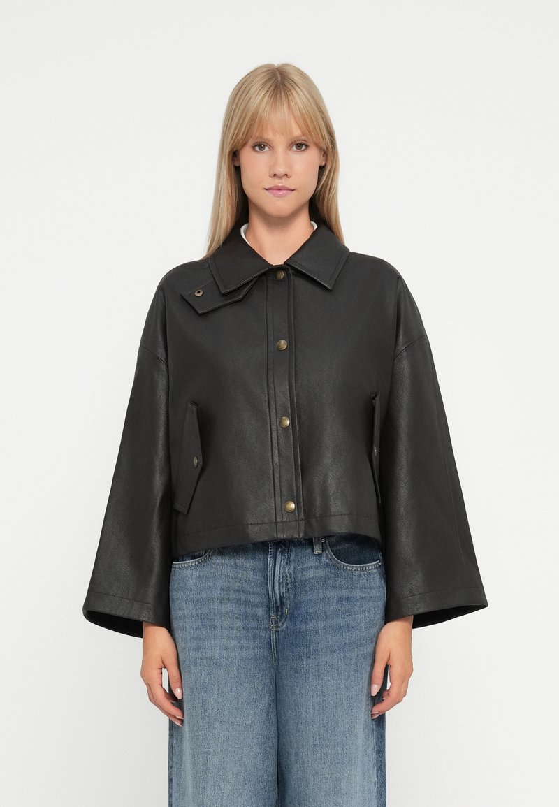 Veste en cuir noir courte avec un large col, fermeture avant par boutons et poches sur les côtés. Texture lisse et manches longues ample.