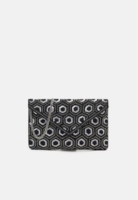 Borsa a busta esagonale in bianco e nero realizzata in paillettes, con tracolla in catena argentata e chiusura a pattina. Forma rettangolare compatta.