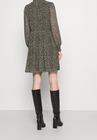 Robe noire à fleurs avec des manches longues transparentes, taille froncée et jupe évasée. Associée à des bottes noires à talons blocs hautes jusqu'aux genoux.