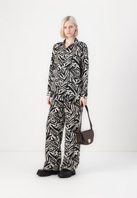 Svart och vit randig zebra-mönstrad skjorta och byxor, med lös passform, tillsammans med en liten brun axelväska och kraftiga svarta skor.