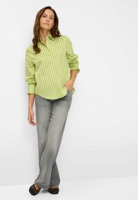 Groen-wit gestreept overhemd met een button-down boord, gecombineerd met grijze broek met rechte pijpen en zwarte, gevlochten instapschoenen.