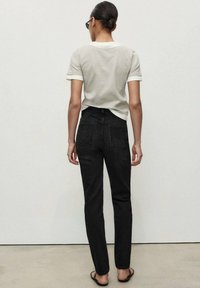 Black jeans with a straight-leg fit and back pockets, paired with a light grey t-shirt. Smooth fabric with a slight sheen. Simple design.