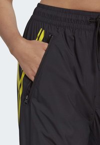 Černé sportovní kalhoty se slim fit, s žlutými akcentními pruhy, zipovými bočními kapsami a elastickým pasem se šňůrkou.