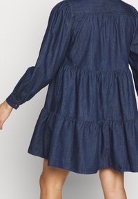 Tummansininen mekko, jossa on pitkät hihat, ansatsit ja joustavat hihansuut. Mekossa on sovitettu yläosa ja levenevä hame.