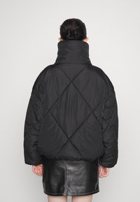 Chaqueta acolchada negra con cuello alto, patrón de rombos y corte oversized. Usada sobre una minifalda de cuero negra.