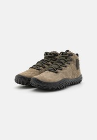 Botas de senderismo con un upper de ante color tostado, suela de goma negra, perfil texturizado y cordones negros y amarillos. Presentan un respaldo elevado y acentos laterales.