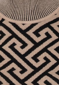Maglione lavorato a maglia con scollatura a coste in beige, caratterizzato da un motivo geometrico nero. La texture è morbida e liscia, che mette in risalto il design.