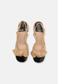 Beige bőr slingback cipők masni dísszel, fekete lakk orral és texturált talpbetéttel. Alacsony sarokkal és állítható pánttal rendelkezik.