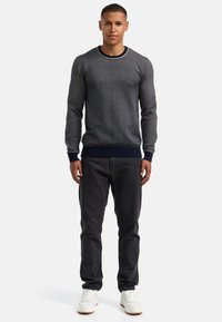 Grå strikkegenser med teksturert mønster, marineblå ribbet mansjetter og kant, rund hals med et subtilt preg. Kombinert med mørke jeans og hvite joggesko.