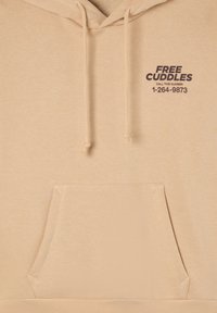 Beżowa bluza z kapturem, wykonana z miękkiego materiału. Posiada kieszeń z przodu, sznurki do regulacji oraz napis "DARMOWE PRZYTULENIA" w ciemno-brązowym kolorze.