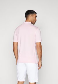 Ljust rosa polo-shirt i mjukt tyg med korta ärmar, krage och sidofickor, kombinerad med vita shorts.