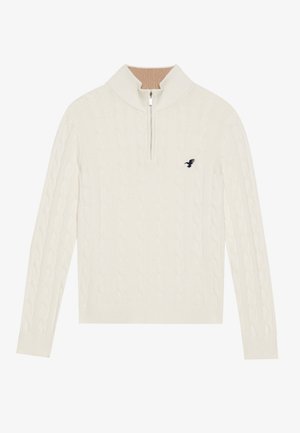 Weißer Kabelstrick-Pullover mit hohem Kragen, halber Reißverschluss vorne und einem kleinen schwarzen Logo-Detail auf der linken Brust.