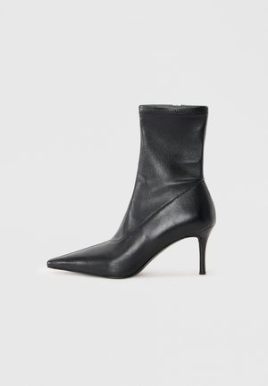 Bottine noire en cuir avec un bout pointu, un talon aiguille fin et un dessus ajusté en forme de chaussette. Texture lisse avec un minimum de détails de couture.