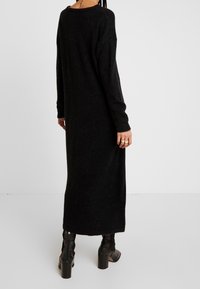 Robe longue en maille noire à coupe décontractée, tissu texturé, encolure ronde et manches longues, associée à des bottines à talons.