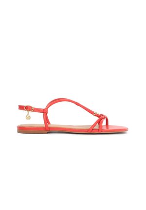 Crvene ravne sandale od glatkog materijala, s tankim trakama, T-bar dizajnom i zlatnim amuletom na remenu oko zapešća.