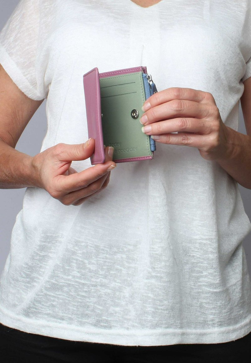 Compact wallet featuring a pink exterior, green interior, card slots, and a zippered pocket. Material appears to be smooth leather or synthetics.