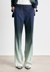 Ombre-Hosen, die von dunkelblau zu hellgrün übergehen, aus glattem Stoff gefertigt. Sie besitzen eine taillierte Passform mit Vorderfalten und seitlichen Taschen.