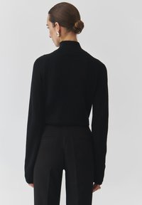 Černý pletený svetr s vysokým výstřihem, dlouhými rukávy a zkráceným střihem, spárovaný s elegantními černými kalhotami. Jednoduchý a čistý design.